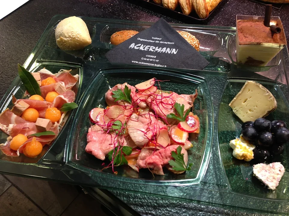 Scène d'extérieur montrant plusieurs gros morceaux de viande fumés suspendus à des crochets métalliques sur une barre en bois