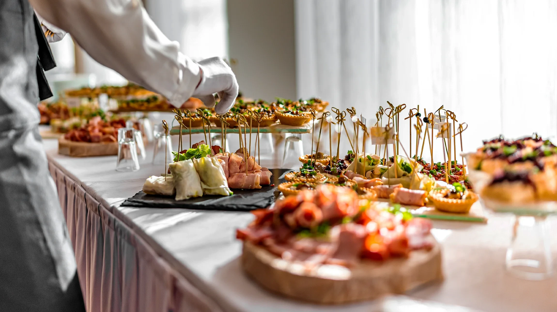 Scène de service traiteur professionnel en intérieur avec personnel en tenue blanche servant muffins et pâtisseries sur buffet