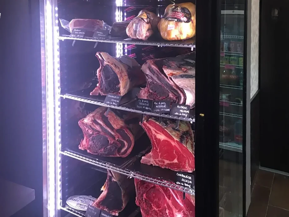 Intérieur d'une boucherie-charcuterie avec comptoir réfrigéré présentant diverses viandes fraîches et charcuteries