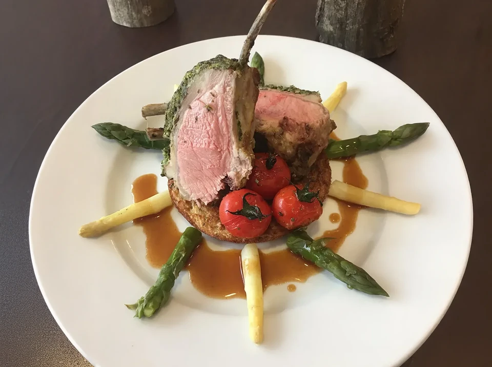 Plat gastronomique servi sur assiette noire avec côtes de porc grillées caramélisées, légumes sautés colorés et sauce de réduction